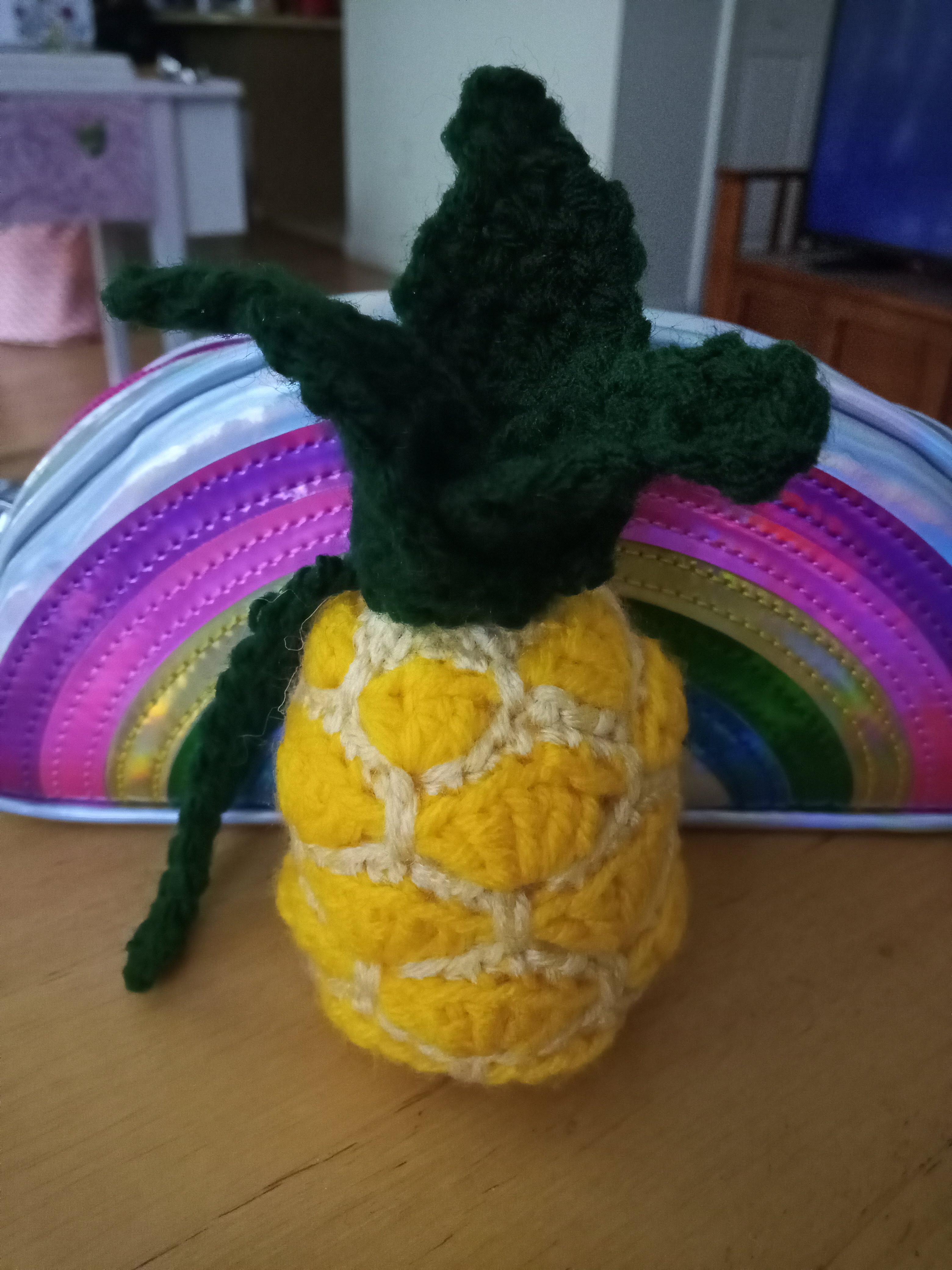 a small crocheted pineapple on a table in front of a rainbow shaped pencil bag