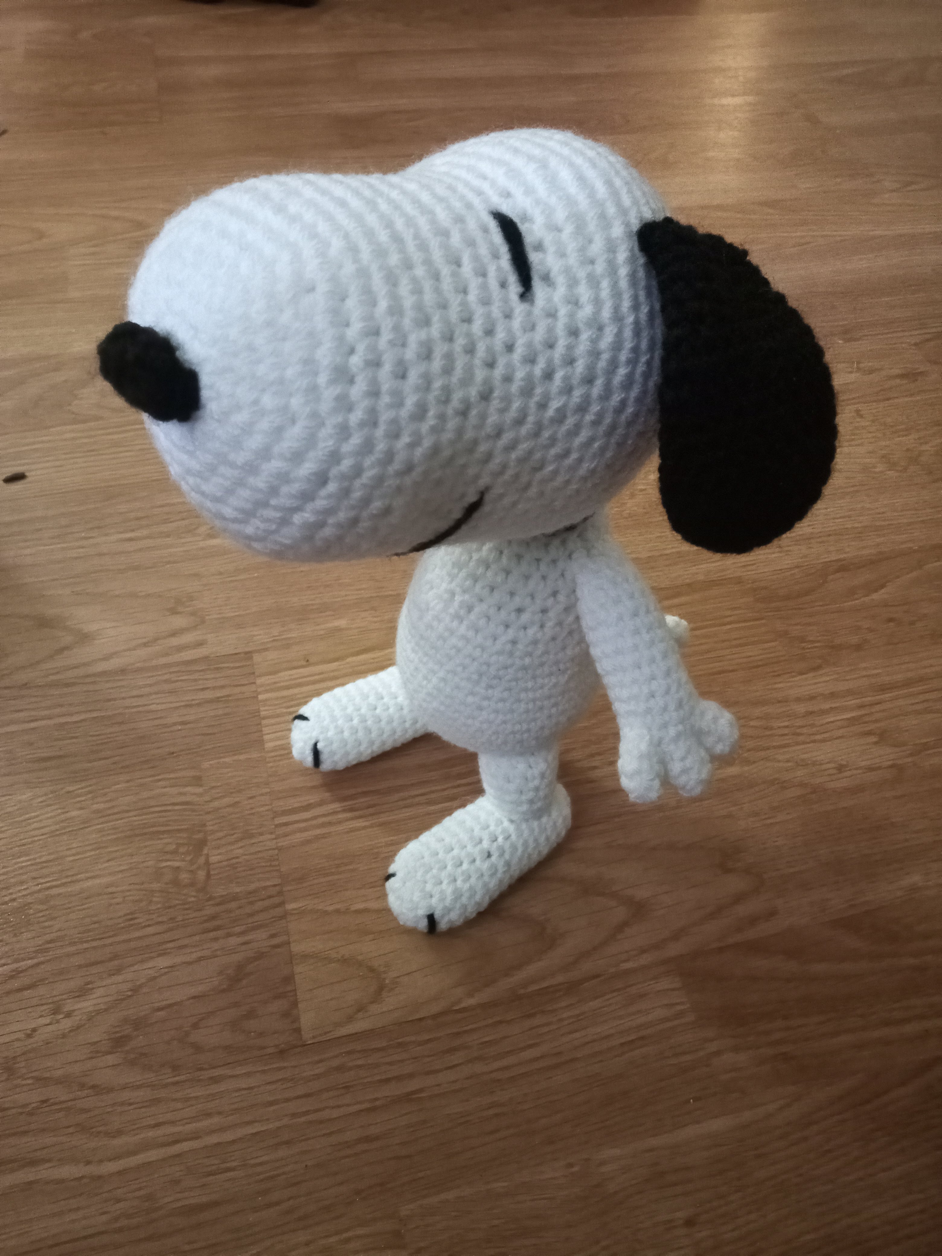 a 3/4 view of a crocheted Snoopy standing on a wooden floor