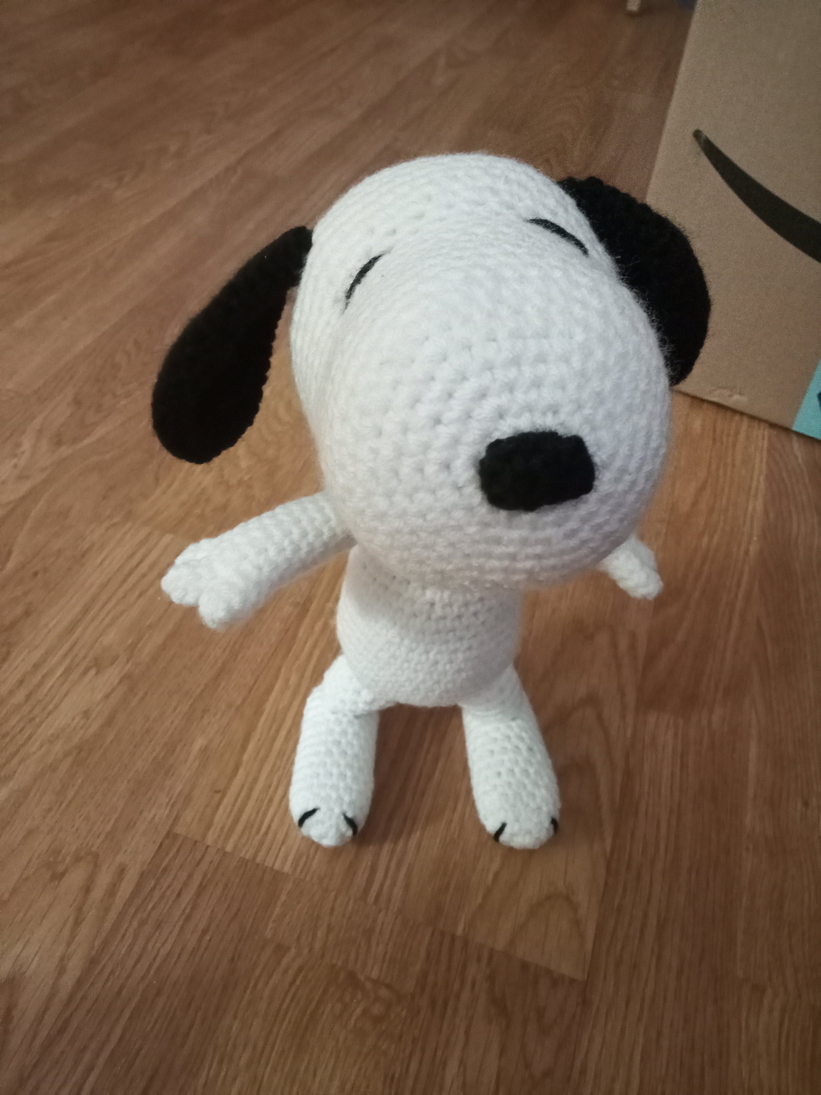 a front view of a crocheted Snoopy standing on a wooden floor