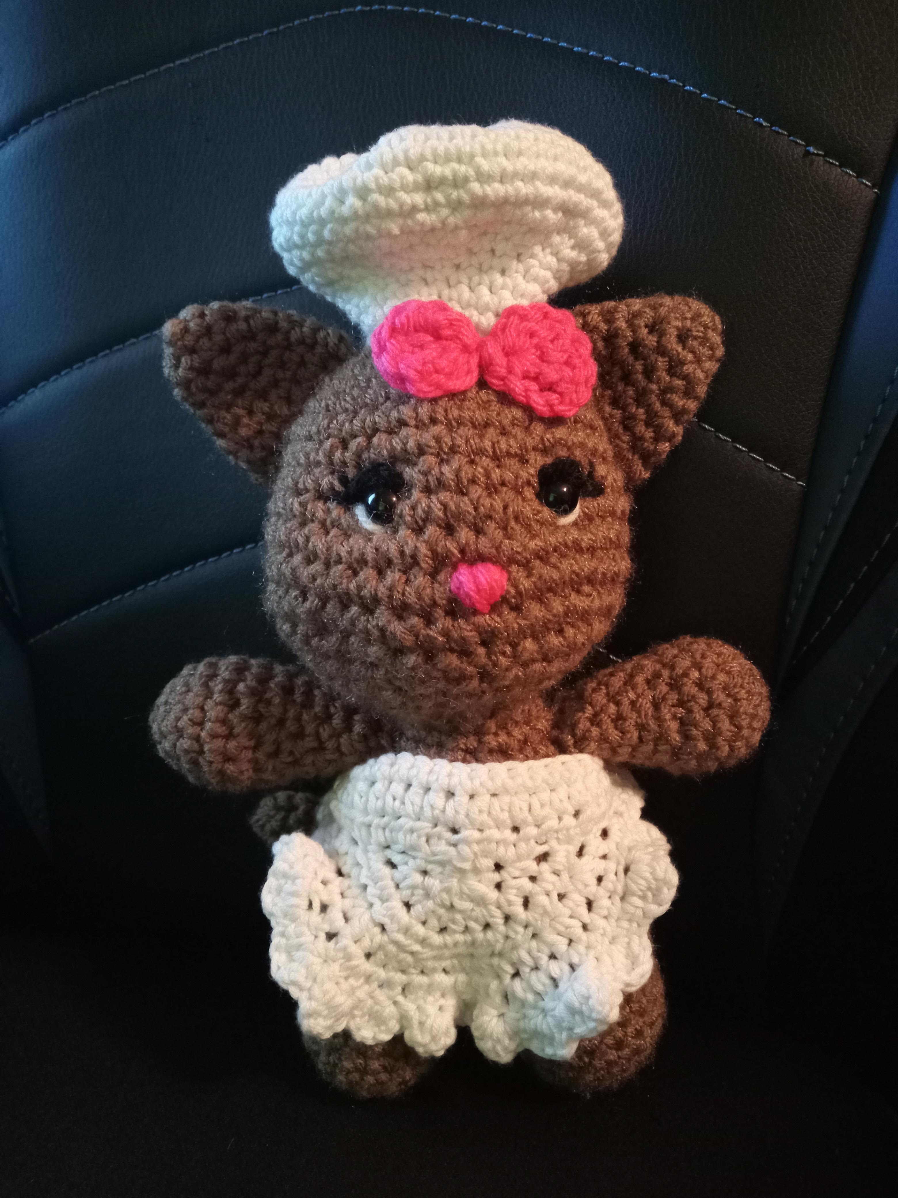 a crocheted brown cat with white lacy apron and chef hat and pink bow