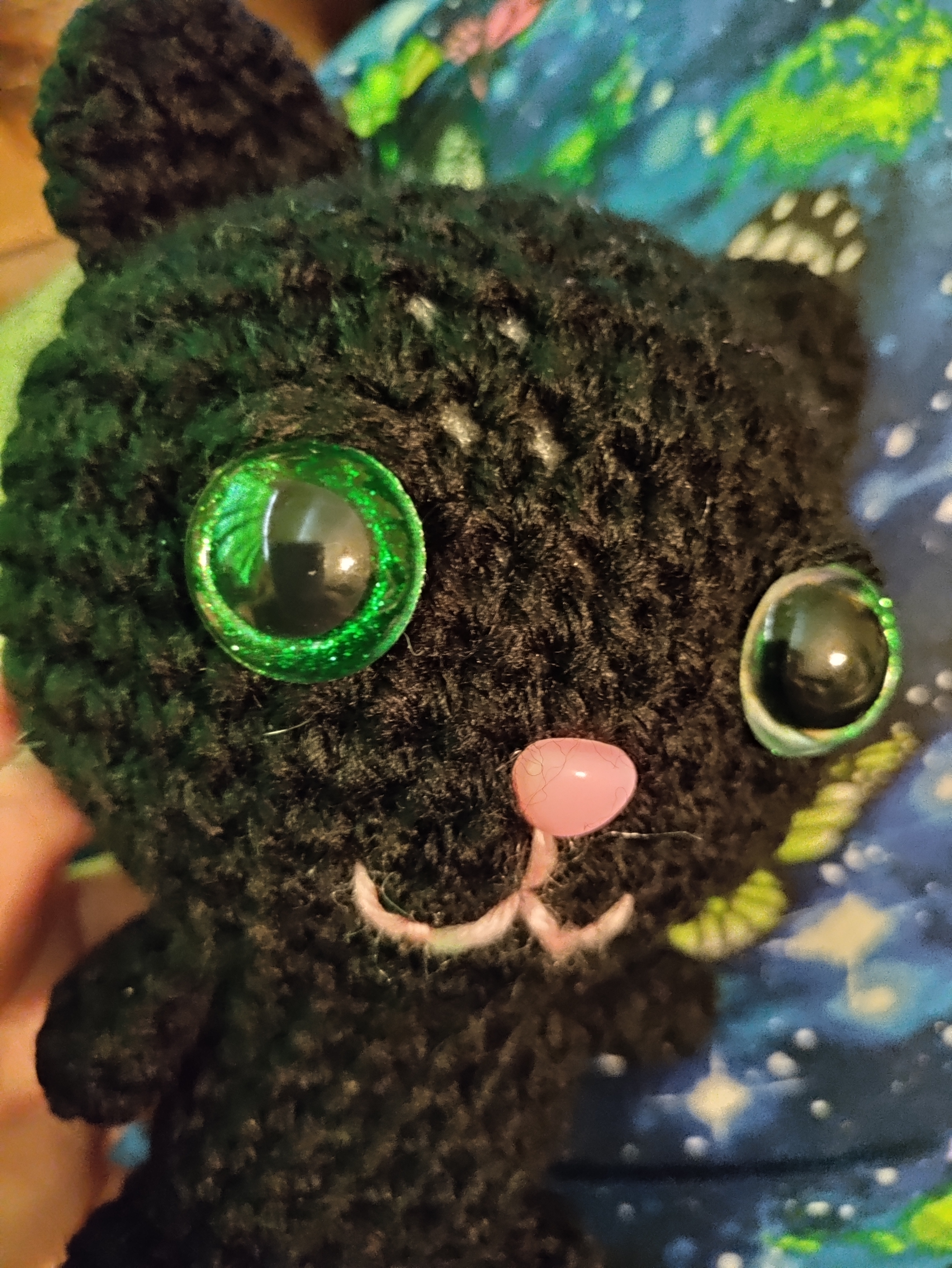 close up of a black cat with glittery green safety eyes and pink nose and mouth