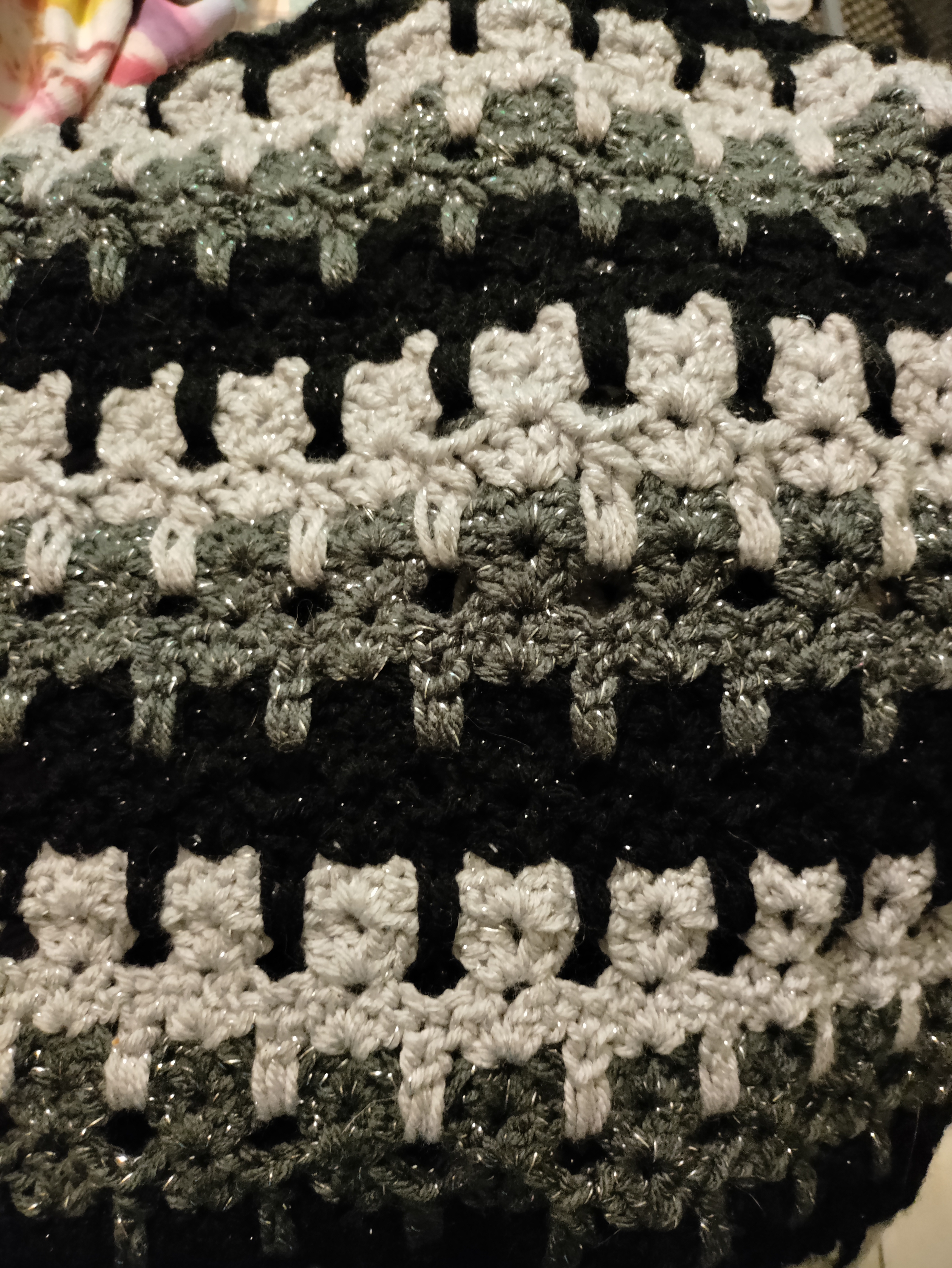 close up of crocheted rows of a cat shaped stitch in alternating rows of glittery silver, dark gray, and black yarns