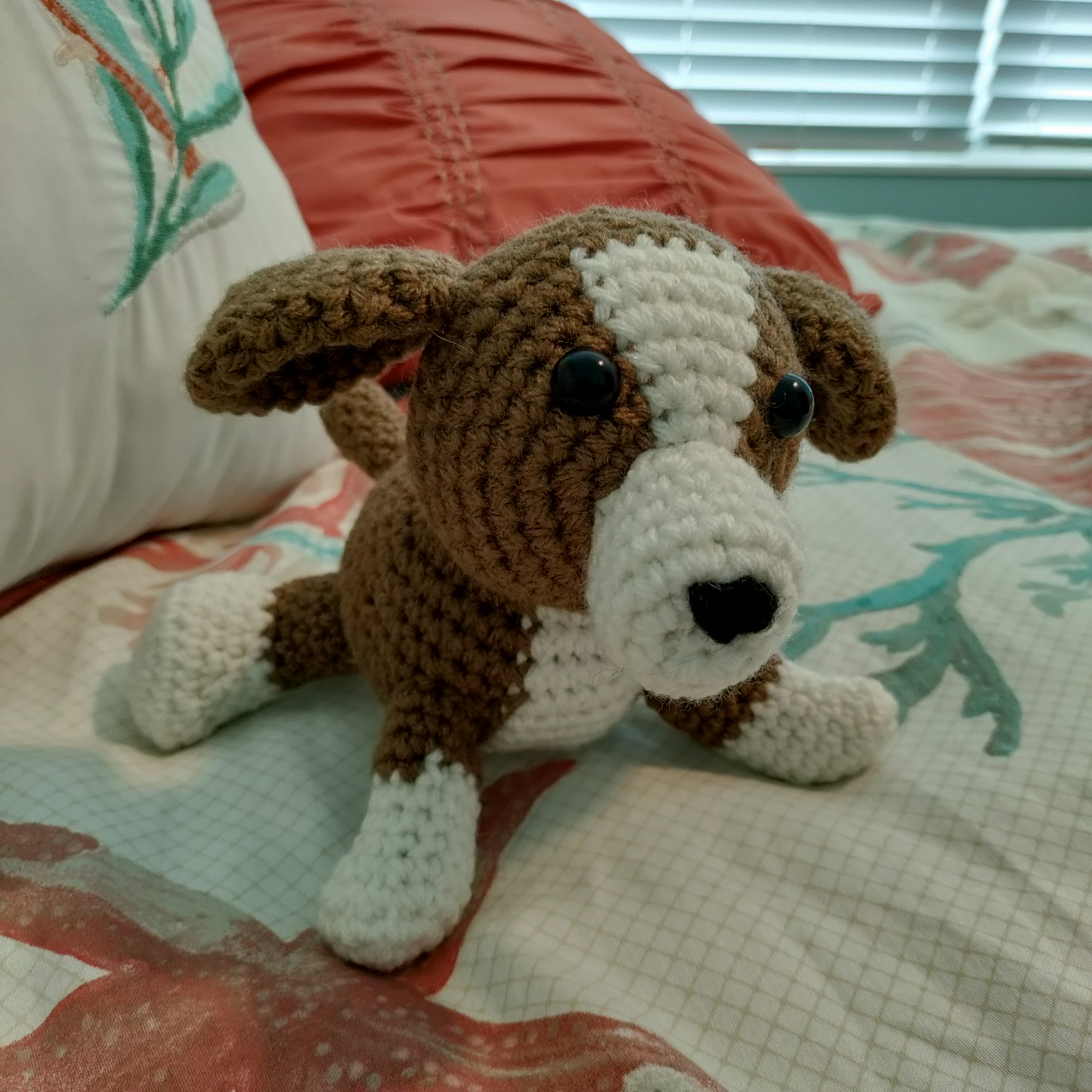 a crocheted brown and white beagle on a blue and coral themed bedspread
