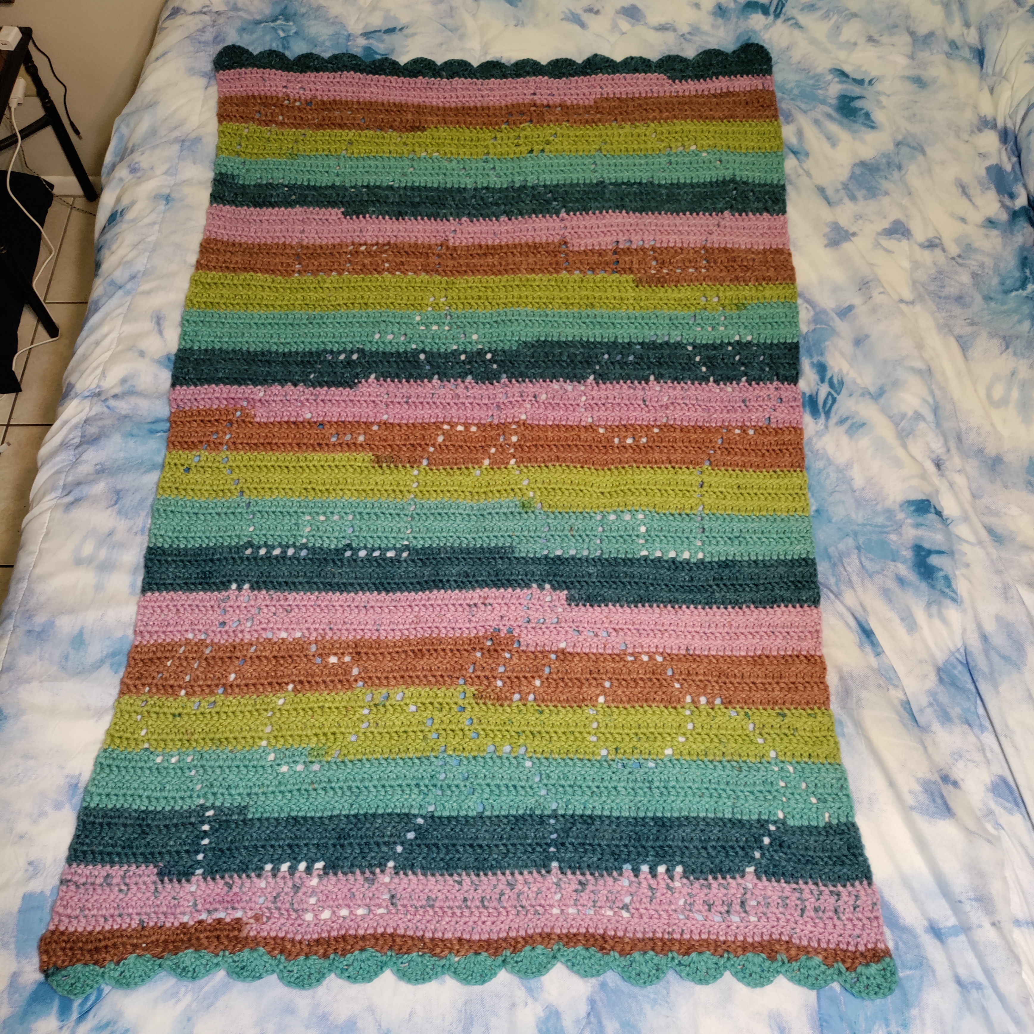 a crocheted blanket with light and dark teals, olive green, brown, and pink stripes that has open stitches shaped like cute elephants with their trunks lifted and hearts above them