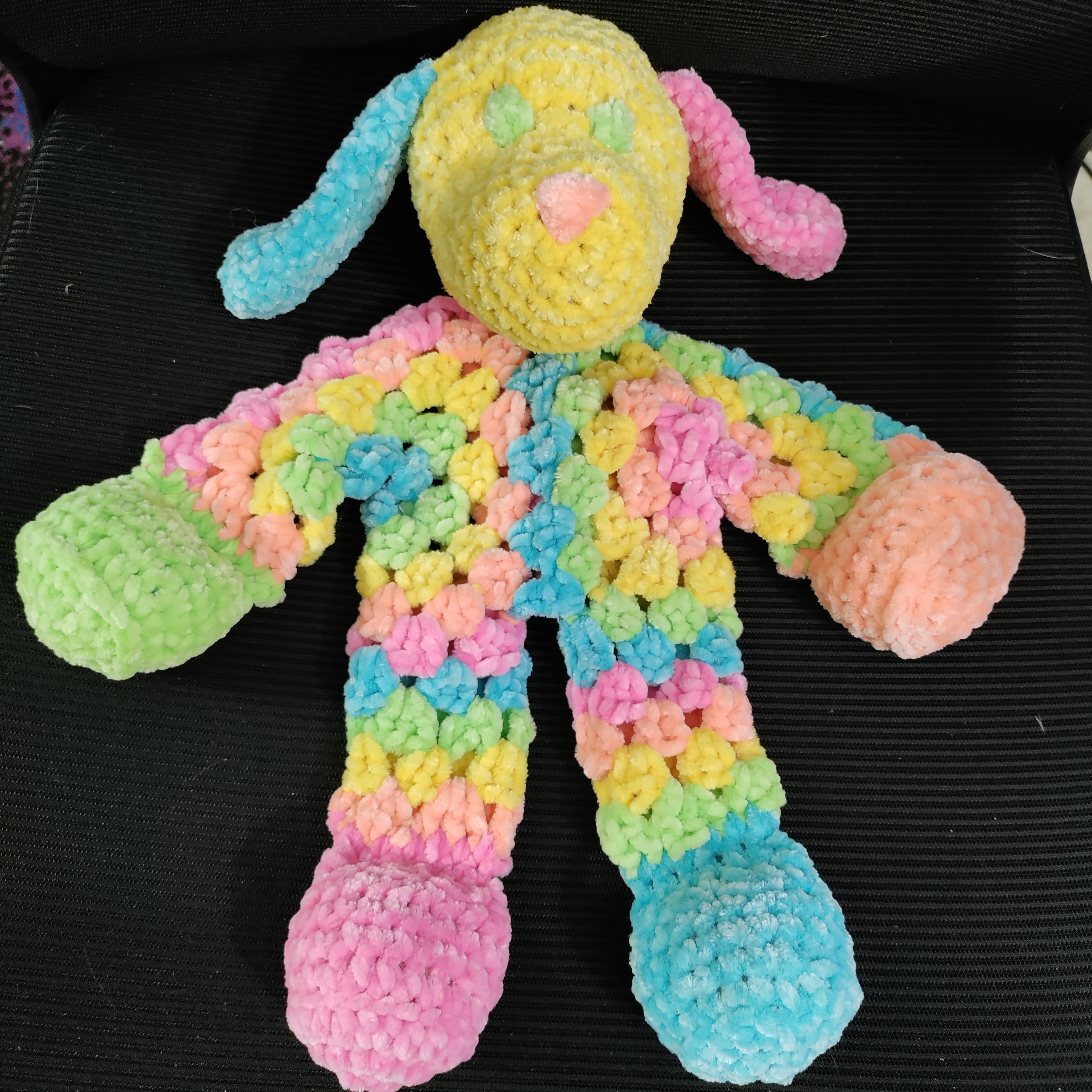 a pastel rainbow striped crocheted dog with different color ears and paws