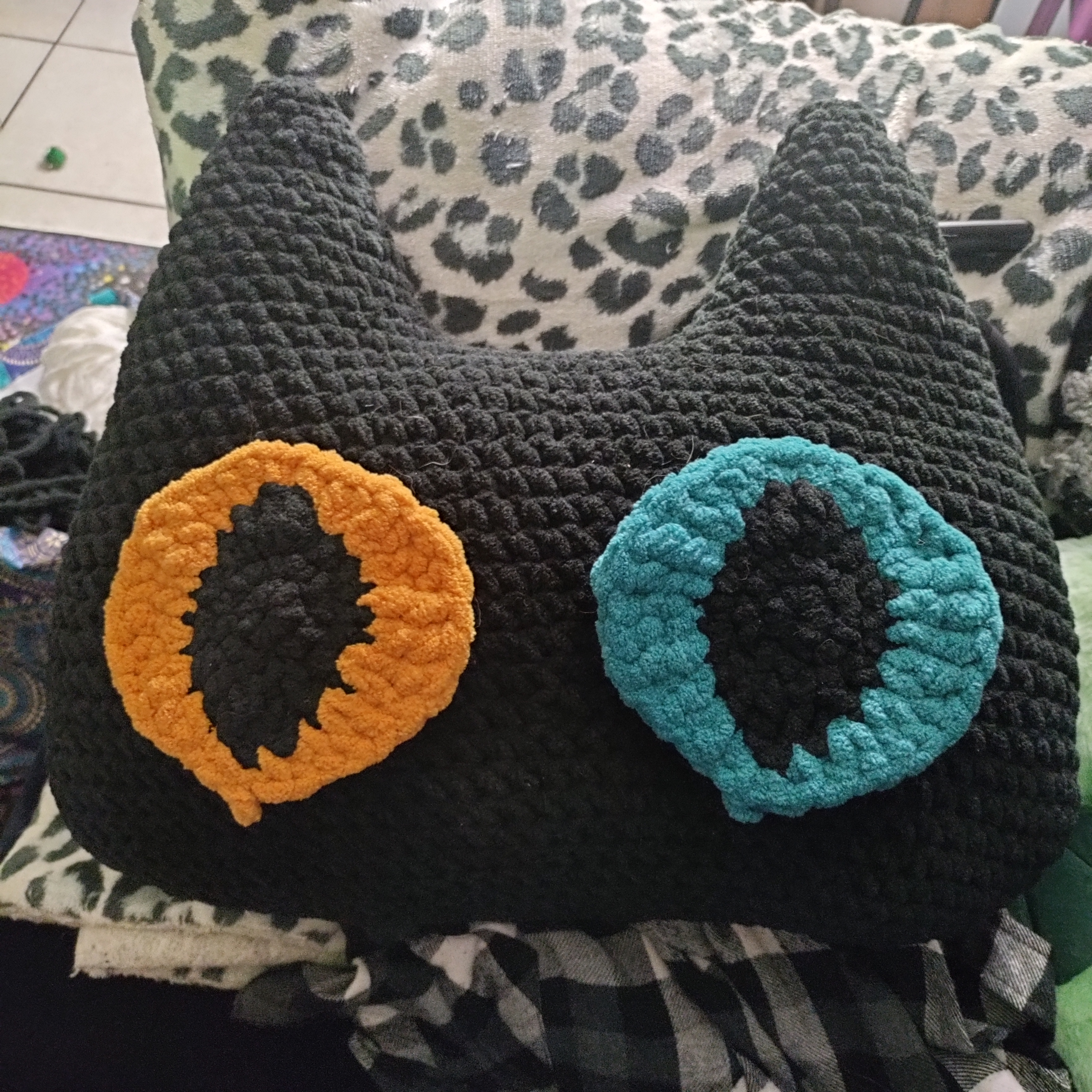 a large crocheted black cat head with one golden yellow eye and one teal eye