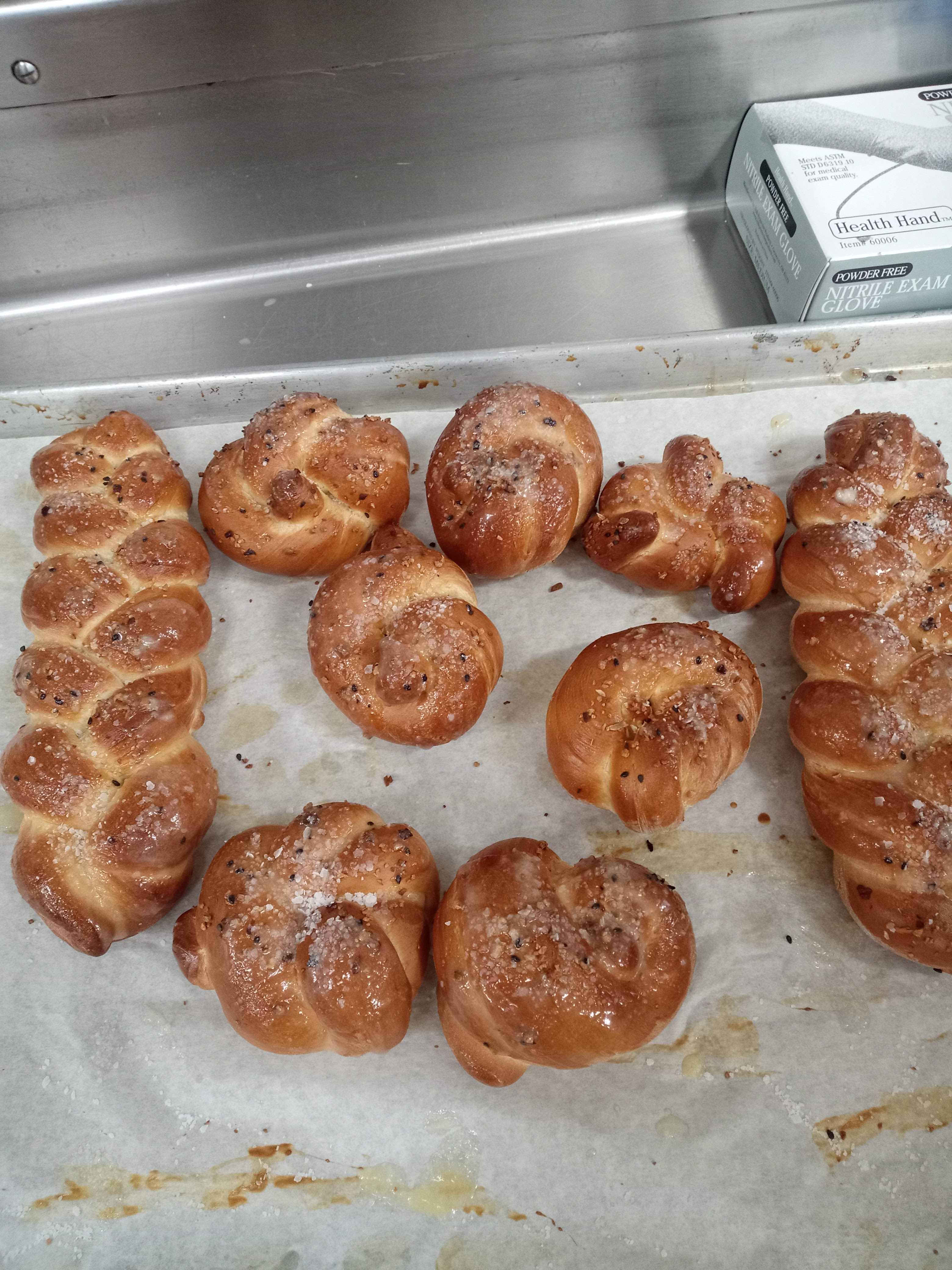 two braided bread loaves and several knotted bread rolls all salted and golden brown on top of a parchment paper covered baking sheet
