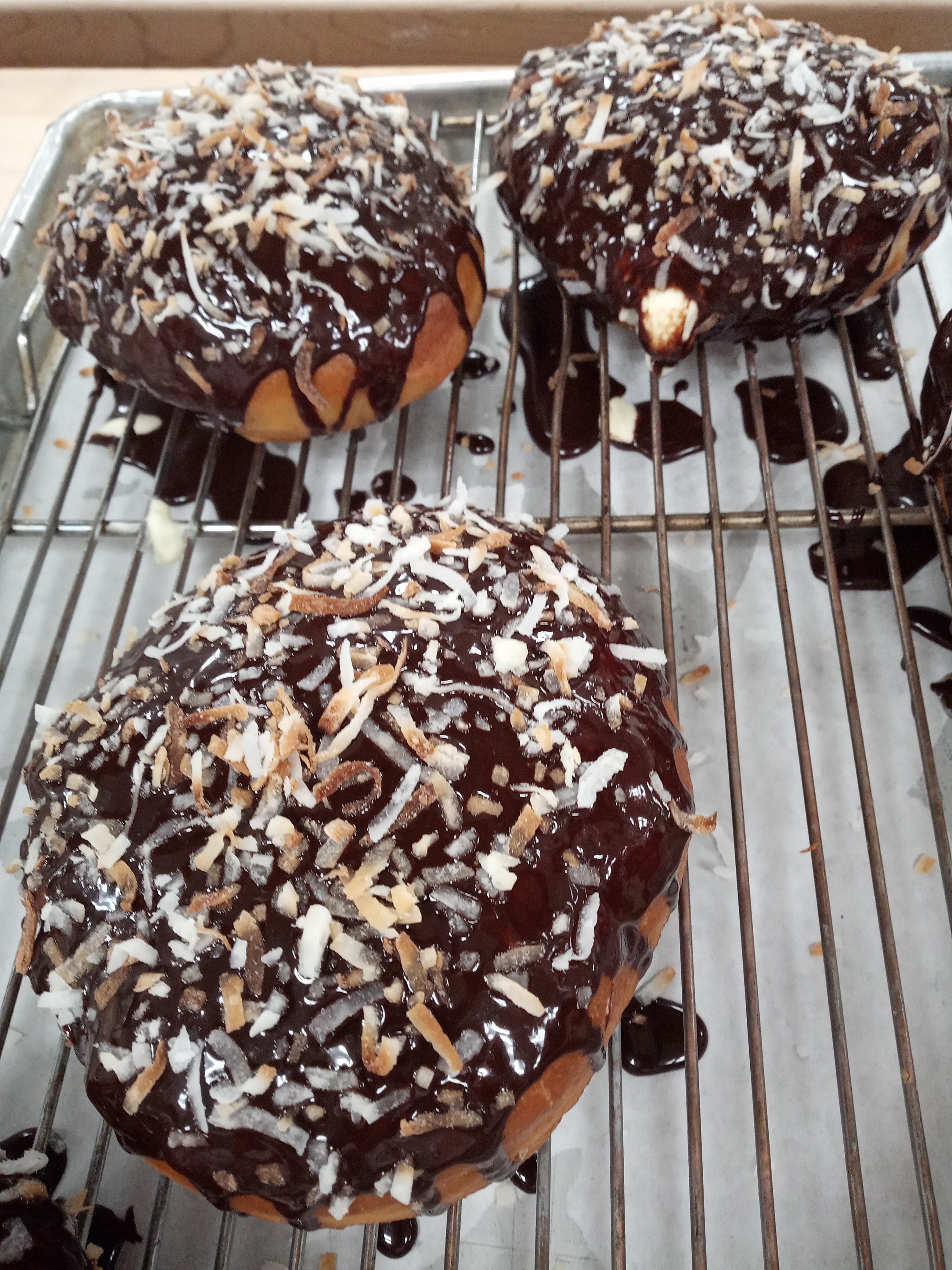 Filled doughnuts covered with chocolate and toasted coconut on top of a wire rack covered sheet tray