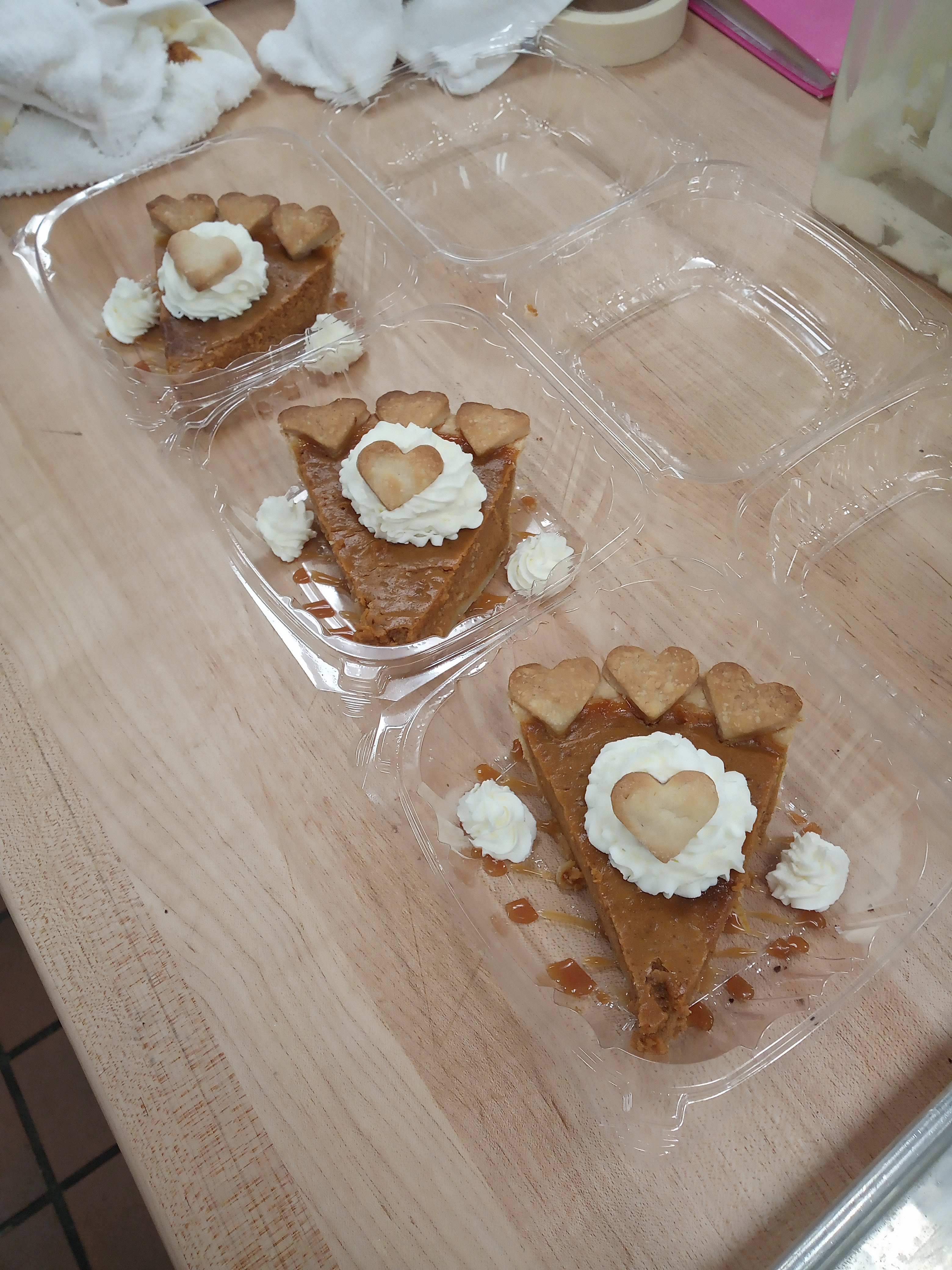 three slices of pumpkin pie with heart cutouts on the crust and on top of whipped cream garnish all in clear takeout containers