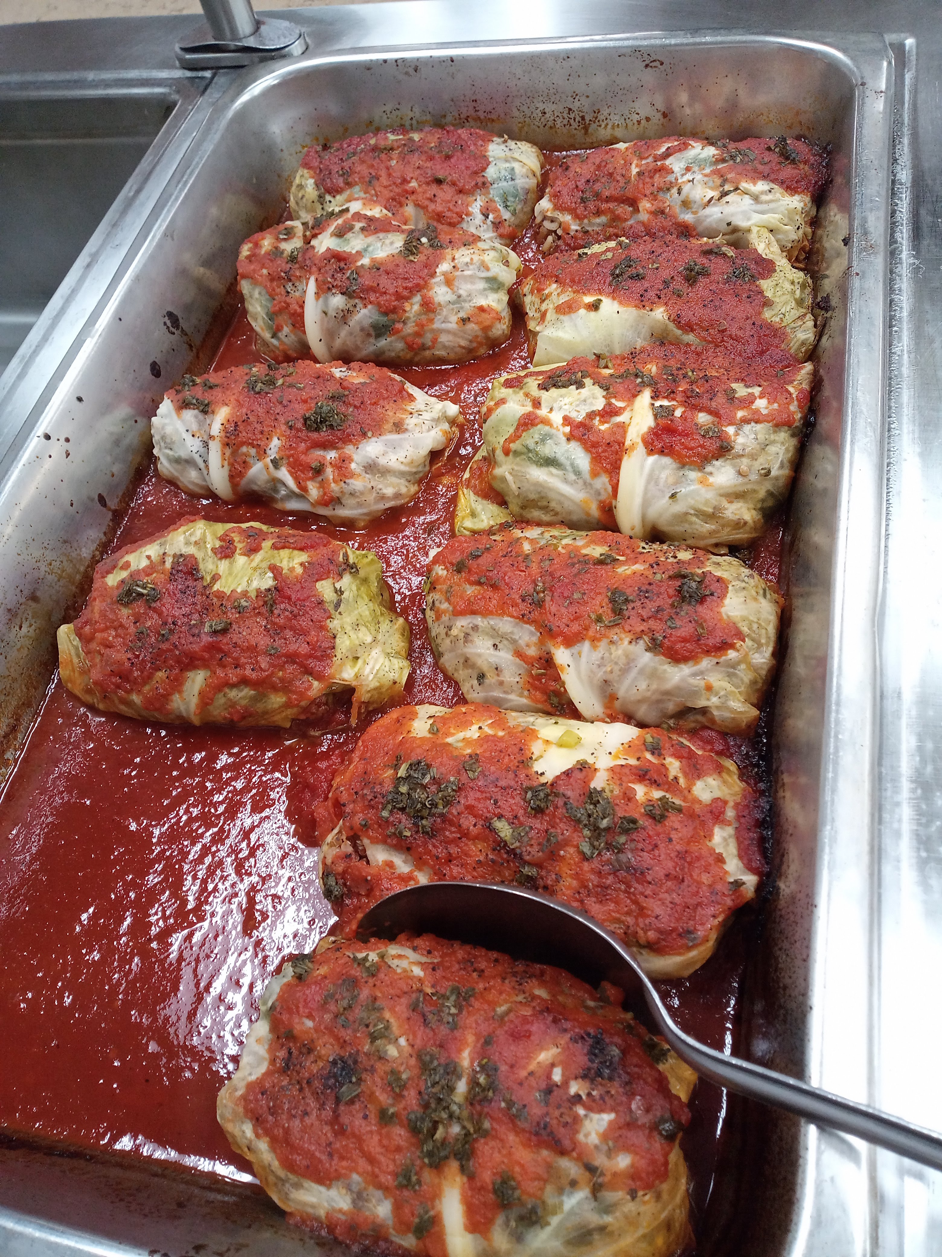 a metal hotel pan filled with stuffed cabbage rolls topped with red tomato sauce