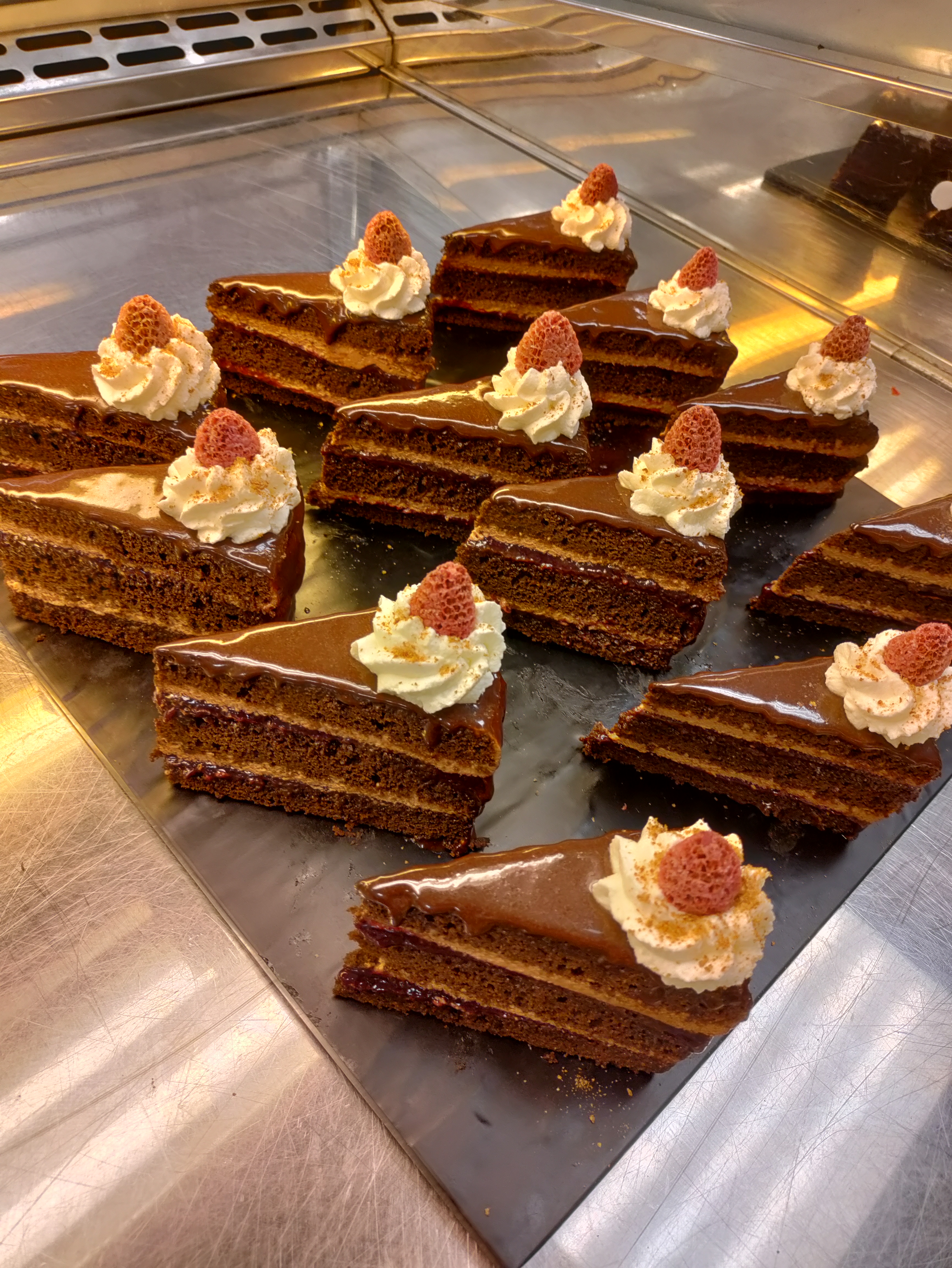 slices of layered chocolate cakes topped with a shiny chocolate glaze and garnished with whipped cream and freeze dried raspberries