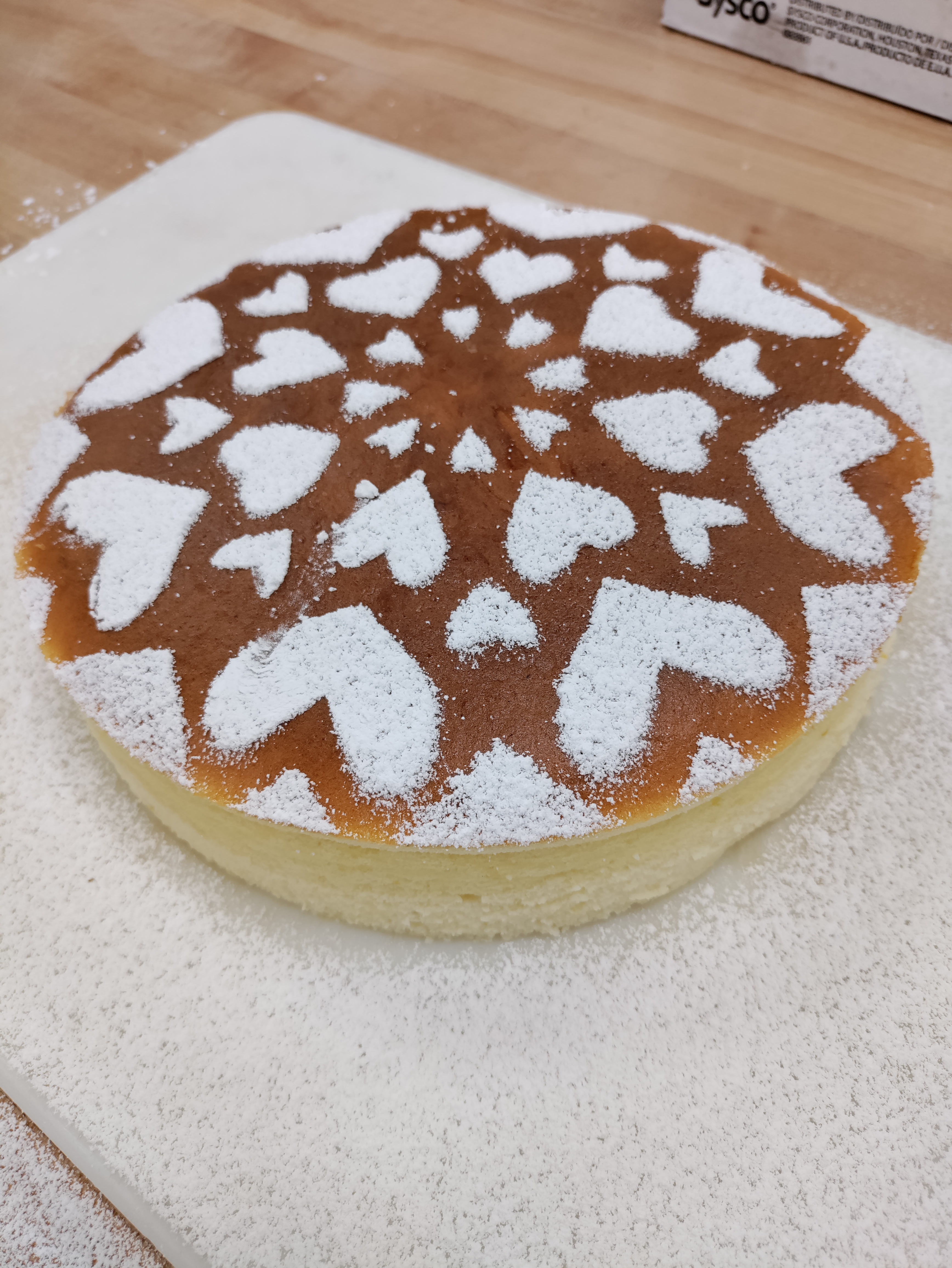 a cheesecake with a golden top crust covered in a repeating heart powder sugar design