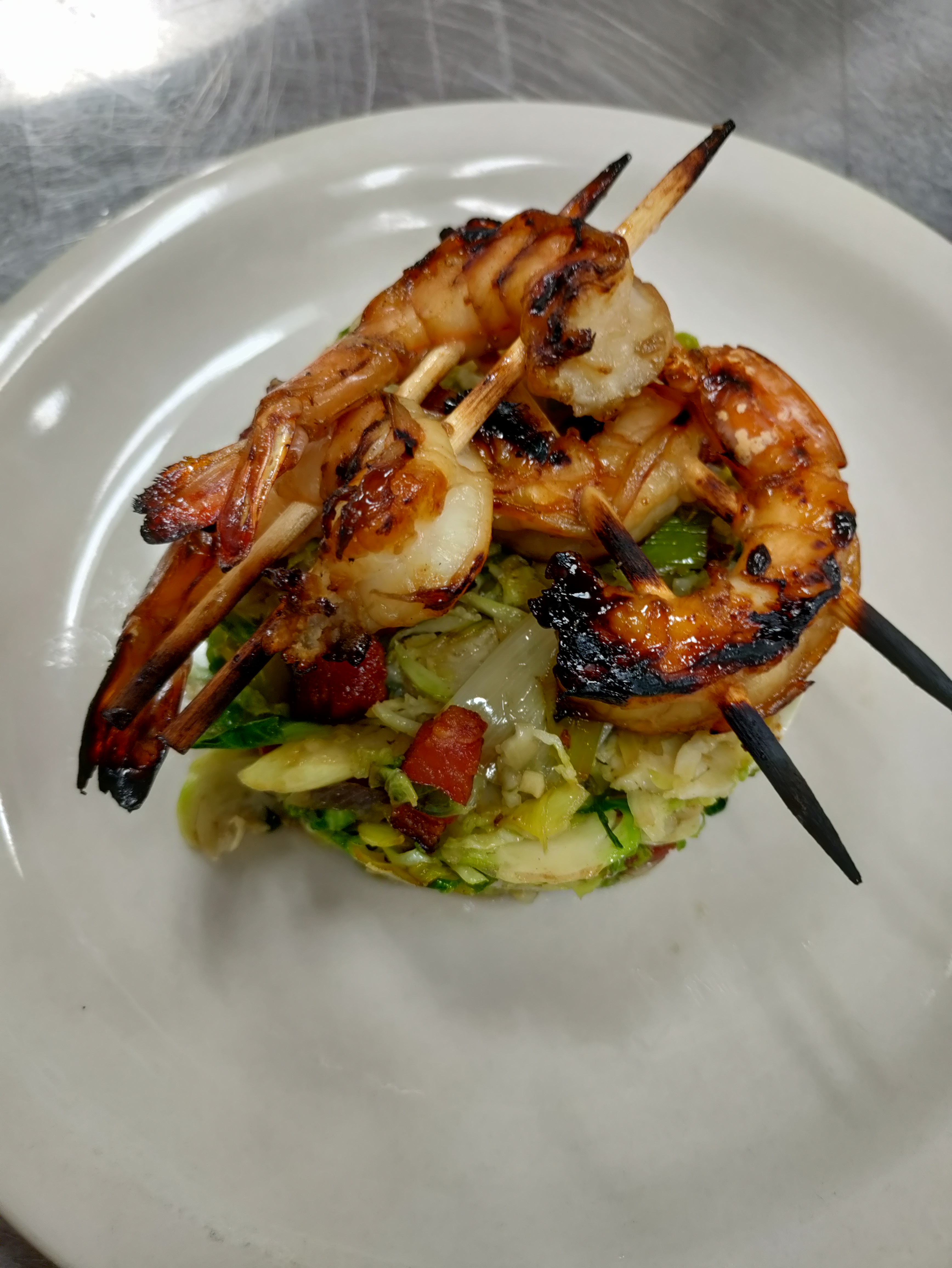 skewered grilled shrimp resting on top of a neat mound of green slaw dotted with bacon bits