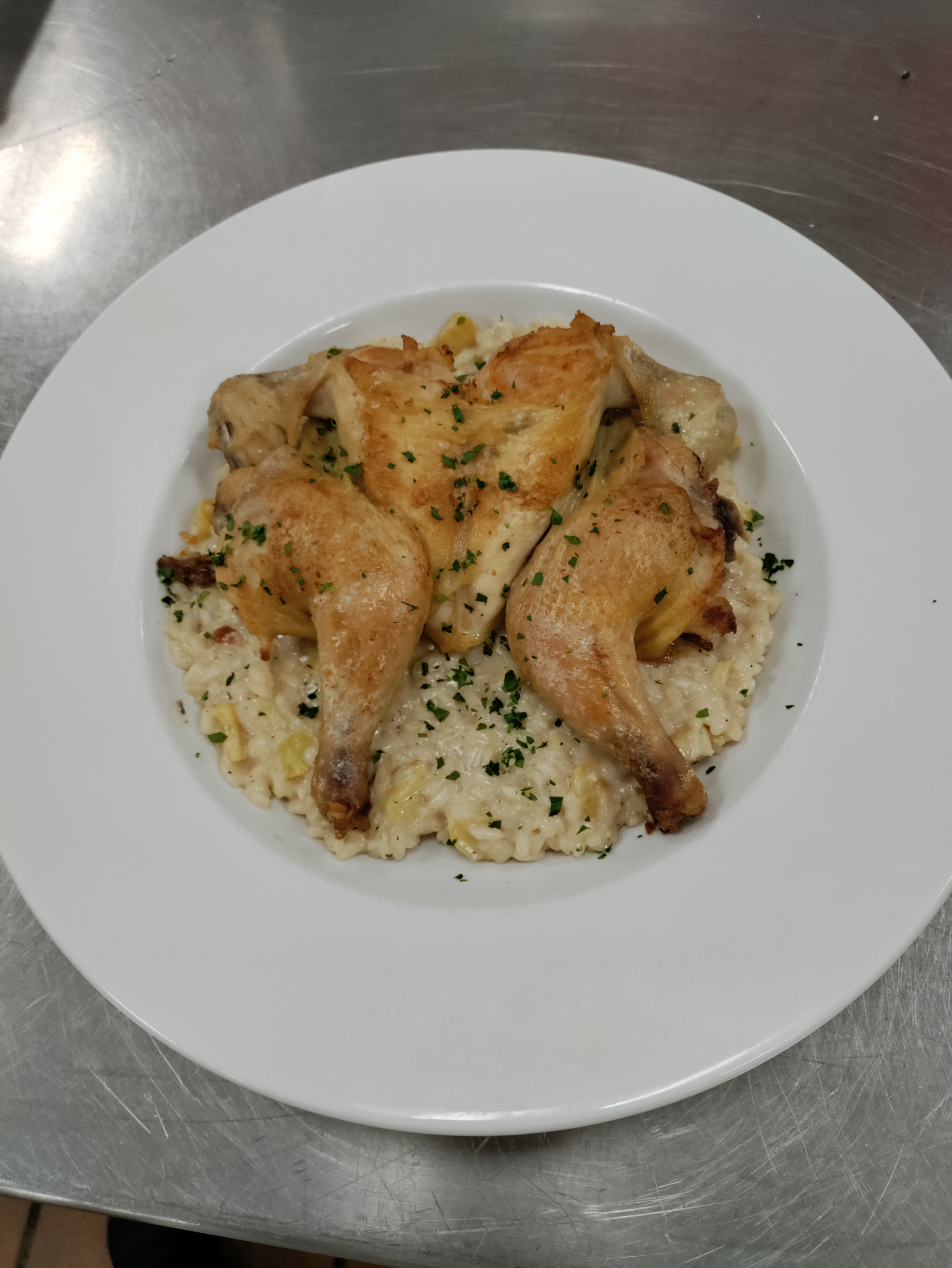 a spatchcocked roasted cornish hen on top of a bowl of risotto garnished with minced parsley